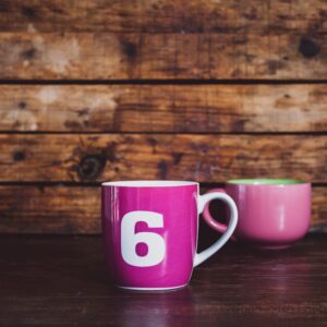Bright pink ceramic mugs with number six design on a rustic wooden surface.